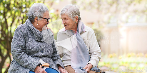 Image of Two elderly women sitting on bench in park smiling happy life long friends enjoying retirement