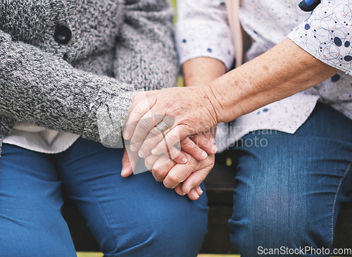 Image of Two elderly women sitting on bench in park holding hands happy life long friends enjoying retirement