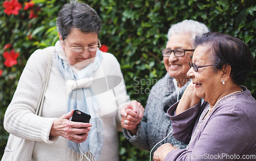 Image of Funny elderly women listening to music on smartphone wearing earphones smiling enjoying fun celebrating retirement together outdoors