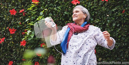 Image of Funny old woman dancing listening to music on smartphone wearing earphones smiling enjoying fun celebrating retirement in garden with flower wall