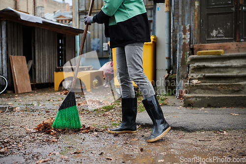 Image of A woman diligently maintains the garden by collecting old, dry leaves, creating a picturesque scene of outdoor care and seasonal tidiness