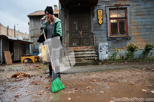 Image of A woman diligently maintains the garden by collecting old, dry leaves, creating a picturesque scene of outdoor care and seasonal tidiness