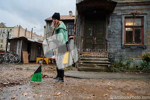 Image of A woman diligently maintains the garden by collecting old, dry leaves, creating a picturesque scene of outdoor care and seasonal tidiness