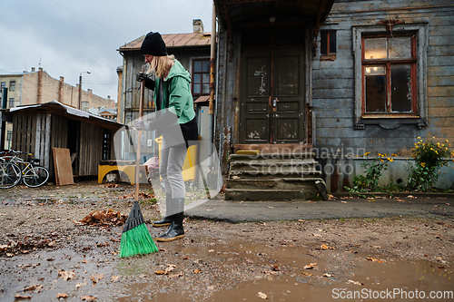 Image of A woman diligently maintains the garden by collecting old, dry leaves, creating a picturesque scene of outdoor care and seasonal tidiness