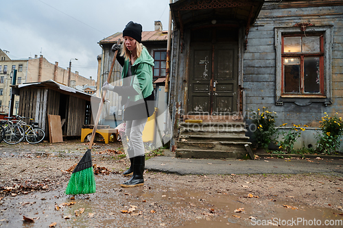 Image of A woman diligently maintains the garden by collecting old, dry leaves, creating a picturesque scene of outdoor care and seasonal tidiness