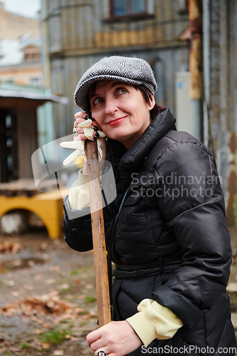 Image of A woman diligently maintains the garden by collecting old, dry leaves, creating a picturesque scene of outdoor care and seasonal tidiness