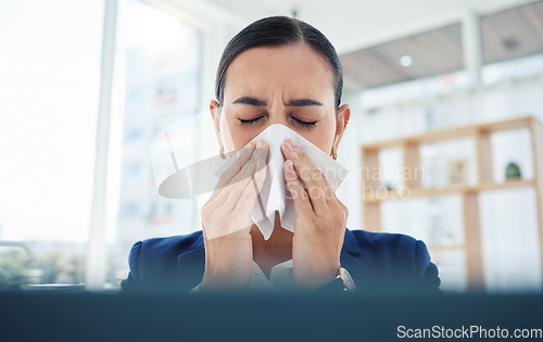 Image of Covid, virus and sick with a business woman blowing her nose with a tissue and sneezing while working in her office. Allergies, sneeze and flu with a female employee suffering from a cold at work