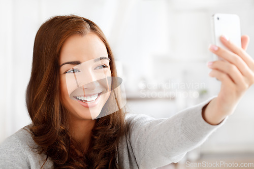 Image of Selfie, phone and social media with a young woman taking a picture or photograph on her smartphone for her online status or timeline. Happy female posing for a photo in a home with mobile technology