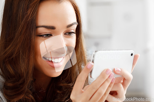 Image of Happy woman watching videos with a phone with an internet app online to stream or download. Young lady smiling while reading a funny meme or enjoying a web series or movie with a smartphone at home