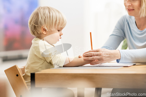 Image of Caring young Caucasian mother and small son drawing painting in notebook at home together. Loving mom or nanny having fun learning and playing with her little 1,5 year old infant baby boy child.