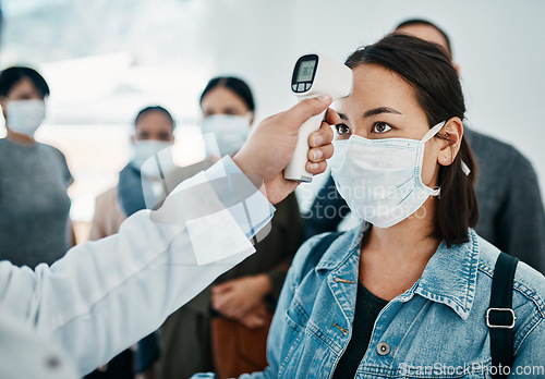 Image of Covid screening with a female tourist in a mask having her temperature taken with an infrared thermometer while waiting to board in an airport. Travel restrictions during the corona virus pandemic
