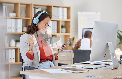 Image of Employee, on phone and headphones in office listening to music while browsing social media. Happy and excited business woman with smile receives good news on her mobile device in corporate building