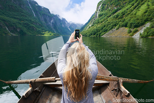 Image of Adventure woman in row boat taking photo on smart phone of beautiful fjord lake for social media