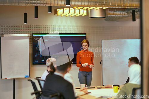 Image of A pregnant business woman with orange hair confidently presents her business plan to colleagues in a modern glass office, embodying entrepreneurship and innovation