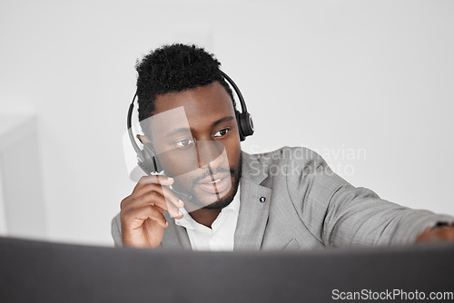 Image of Call center, customer service and crm representative wearing headset while consulting with customer in telemarketing company. Serious black man in contact us and sales support working on a computer