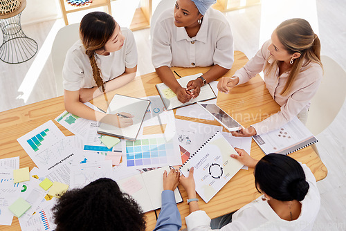 Image of Creative team planning a project with digital tablet and paperwork in corporate office. Top view of professional employees writing notes and analyzing documents with graphs, charts and color wheels.