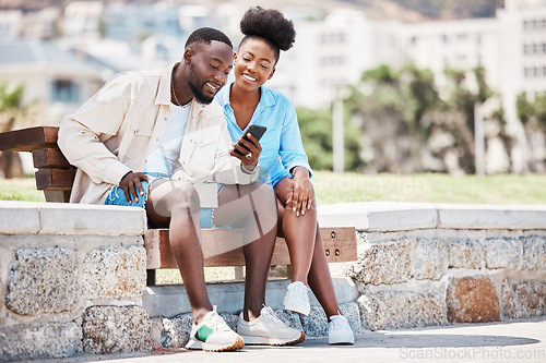 Image of Black couple, love and phone while browsing social media, internet or watching a video while sitting on a park bench. Happy man and woman on a romantic date, trip or summer holiday to relax together