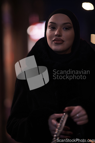 Image of Muslim woman walking on urban city street on a cold winter night wearing hijab