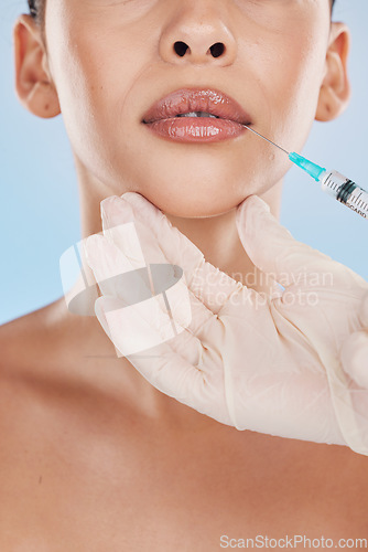 Image of Closeup of a young woman getting lips injection treatment from a cosmetic doctor in a studio. Syringe and needle with lip filler for the mouth by a cosmetology beautician with a blue background.