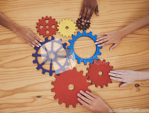 Image of Hands, gears and collaboration with a team of people working with cogs and equipment on a table in the office. Teamwork, synergy and planning with a business group meeting to talk company strategy