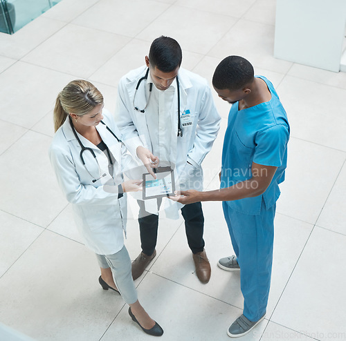 Image of Group of doctors working on digital tablet while standing in the hospital hallway and talking. Top view of healthcare employees analyzing test results and treatment in medicare clinic with technology