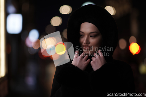 Image of Muslim woman walking on urban city street on a cold winter night wearing hijab