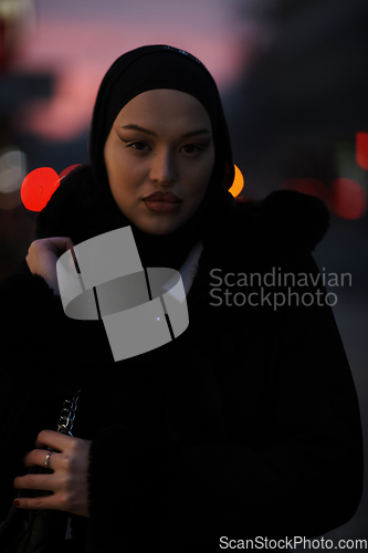 Image of Muslim woman walking on an urban city street on a cold winter night wearing hijab