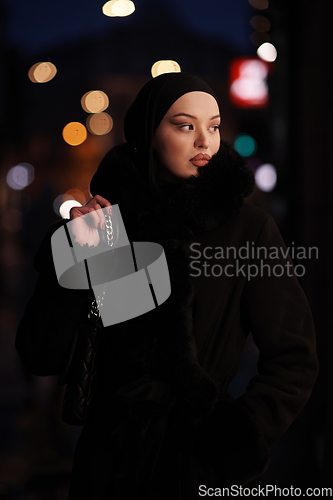 Image of Muslim woman walking on an urban city street on a cold winter night wearing hijab