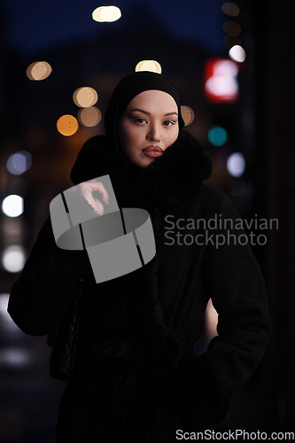 Image of Muslim woman walking on an urban city street on a cold winter night wearing hijab