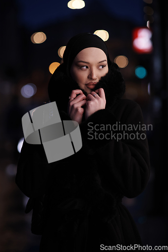 Image of Muslim woman walking on an urban city street on a cold winter night wearing hijab