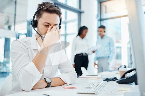 Image of Call center, headache and burnout of a man in customer service or support with eye strain at the office. Business male or employee in telemarketing suffering from head pain at the company workplace.