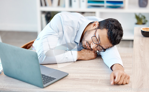 Image of Tired, headache and sleeping worker behind laptop while lying his head on his desk in his office. Stress, burnout and chronic fatigue with young professional male feeling exhausted and overworked