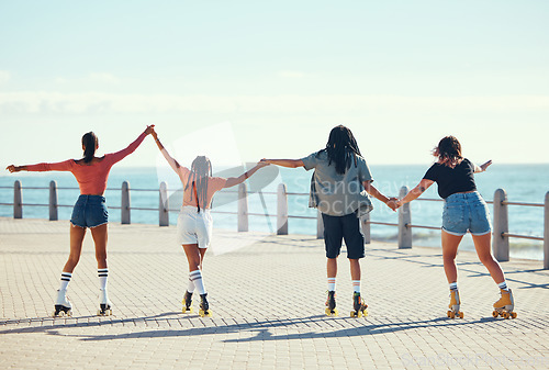 Image of Roller skaters, friends and holding hands at a beach for exercise, fitness and freedom in summer together. Group, male and young girls skating on sidewalk at sea to relax on outdoor holiday vacation