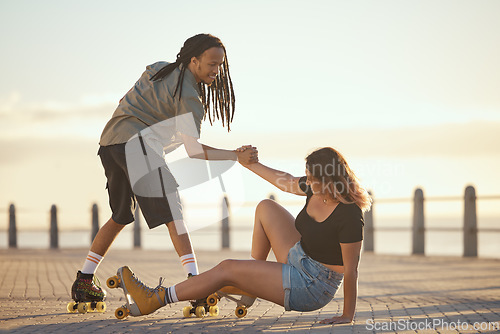 Image of Help, falling and couple roller skating and holding hands at the beach in summer for a fun and healthy cardio activity. Friends love to skate and exercise on sidewalk as girl falls on the ground
