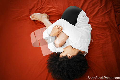 Image of Pain, stomach ache and period with a young woman holding her tummy and curled up while suffering from menstruation symptoms. Sore, hurt or illness with a sick female lying on a bed in her home