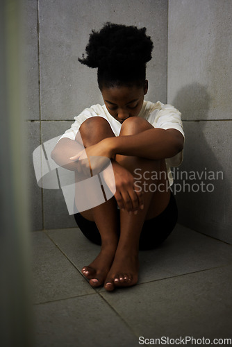 Image of Sad, unhappy and depressed student sitting alone on the floor of a bathroom in school. Lonely, upset and depressed teen girl struggling with bullying and mental health in the corridor