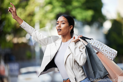 Image of Retail, shopping and taxi with black woman showing hand sign for transport in an urban city. Female shopper looking fashionable with bags of discount sale purchase, waiting for a cab downtown