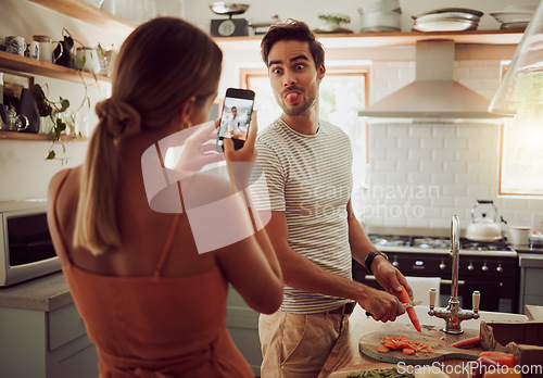 Image of Cooking man sticking out tongue to make silly, goofy and funny face to pose for a photo while making food in the kitchen at home. Crazy, fun and happy couple enjoying a playful moment while bonding