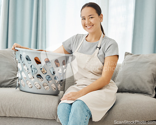 Image of Cleaning, laundry and happy asian woman with on the sofa with a basket about to do washing of fold clothes in the living room at home. Portrait face housewife or maid doing chores and housework