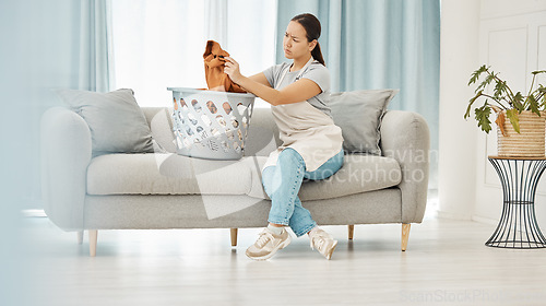 Image of Asian woman, laundry or clothes basket on sofa in house living room and looking confused at dirty stains. Stress, anxiety or worry of person with washing clothing or cleaning fabric in home interior