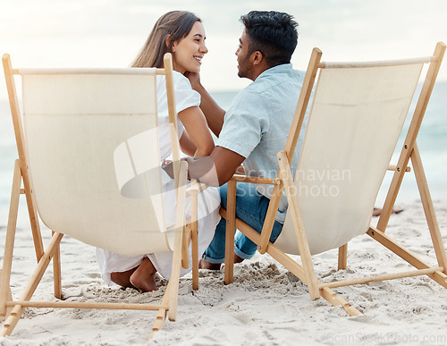 Image of Couple, love and beach vacation of summer holiday with interracial lovers sharing a romantic moment while sitting on chairs in the sand. Happy and young man and woman on tropical honeymoon together