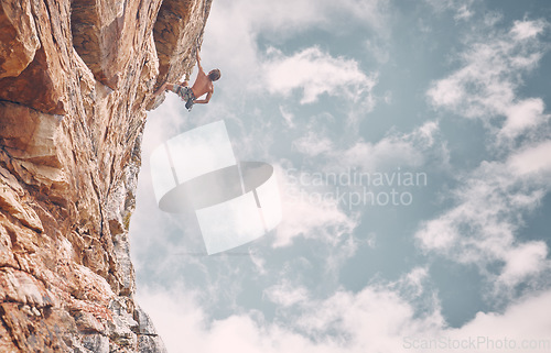 Image of Rock climbing, sports and adventure with man on mountain against a blue sky background for fitness, challenge and training. Motivation, freedom and strong male athlete on cliff for adrenaline