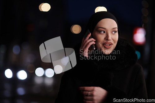 Image of uropean Muslim Hijabi Business Lady checking her phone on urban city street at night