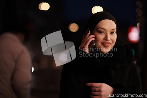 Image of uropean Muslim Hijabi Business Lady checking her phone on urban city street at night