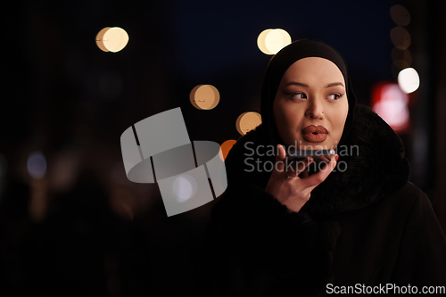Image of uropean Muslim Hijabi Business Lady checking her phone on urban city street at night