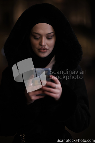 Image of Muslim woman walking on urban city street on a cold winter night wearing hijab