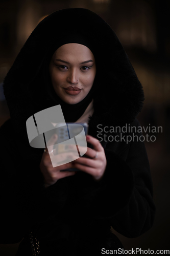 Image of Muslim woman walking on urban city street on a cold winter night wearing hijab