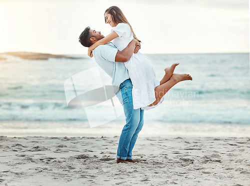 Image of Man at beach lift woman with love, smile with sun setting over the horizon or background. Young couple travel to ocean on vacation, happy together with sunset over sea or waves in nature backdrop.