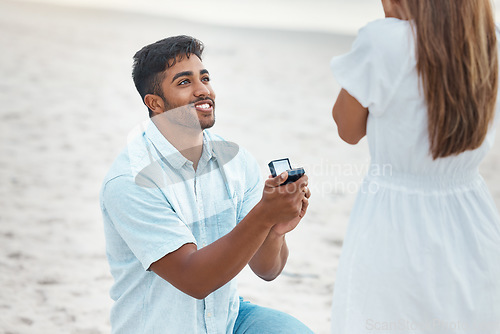 Image of Proposal, surprise and engagement with wedding ring on beach with indian man on knee for love, commitment and marriage. Save the date, gift and diamond jewellery present for woman for romance