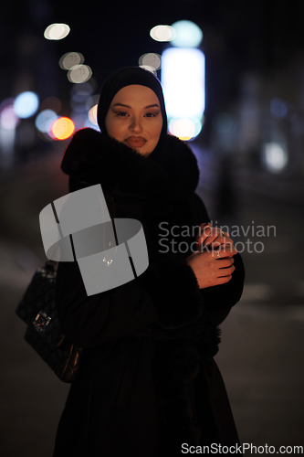 Image of Muslim woman walking on urban city street on a cold winter night wearing hijab